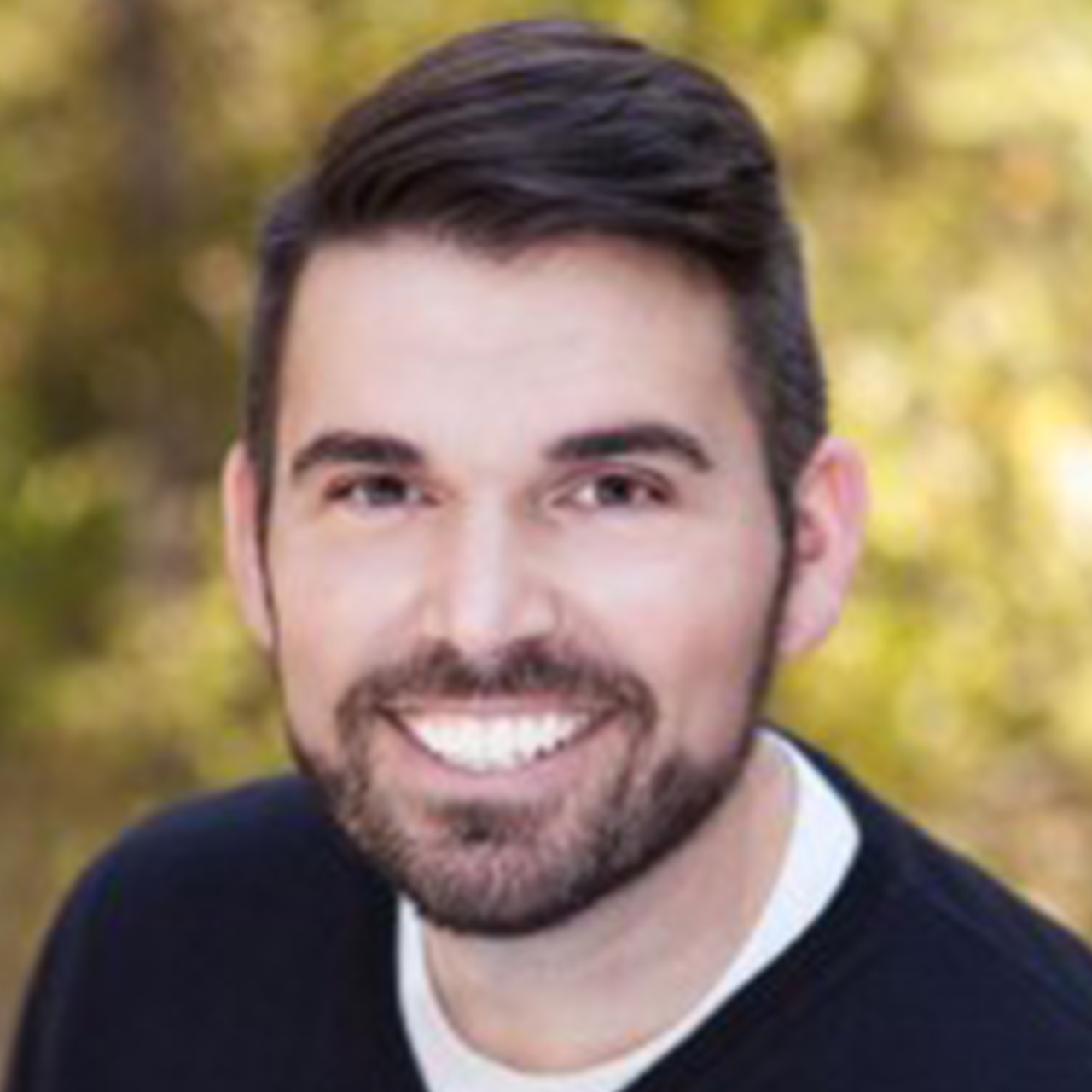 man with dark hair and beard wearing a black sweater with a white shirt underneath