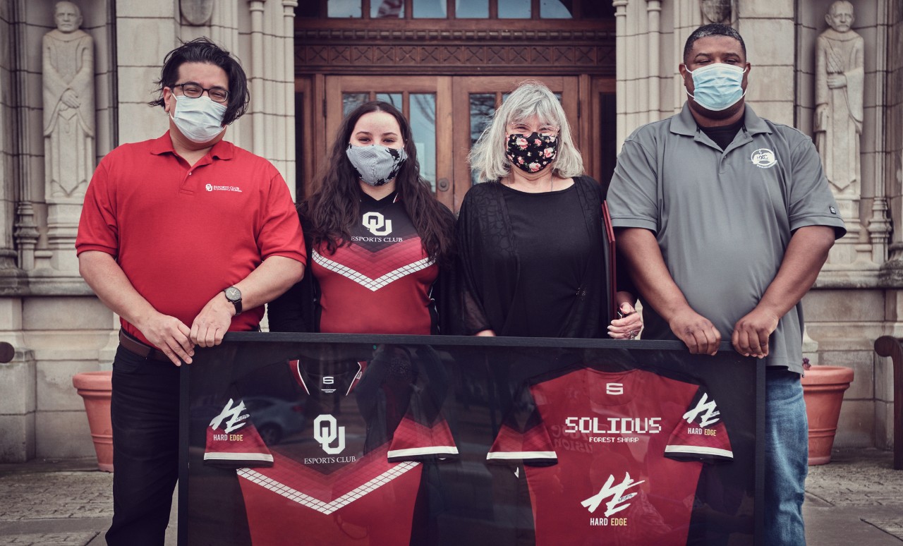 On March 1, 2021, Michael Aguilar, Director of Esports & Co-Curricular Innovation, Kara Brightwell, Community Outreach Coordinator of The OU Esports Club, and Ricky McNeal Founder and CEO of HXC Gaming Events presented a tribute jersey set for Forest "Solidus" Sharp to his mother Gretchen "Momma Solidus" Evans in front of Evans Hall at The University of Oklahoma. 