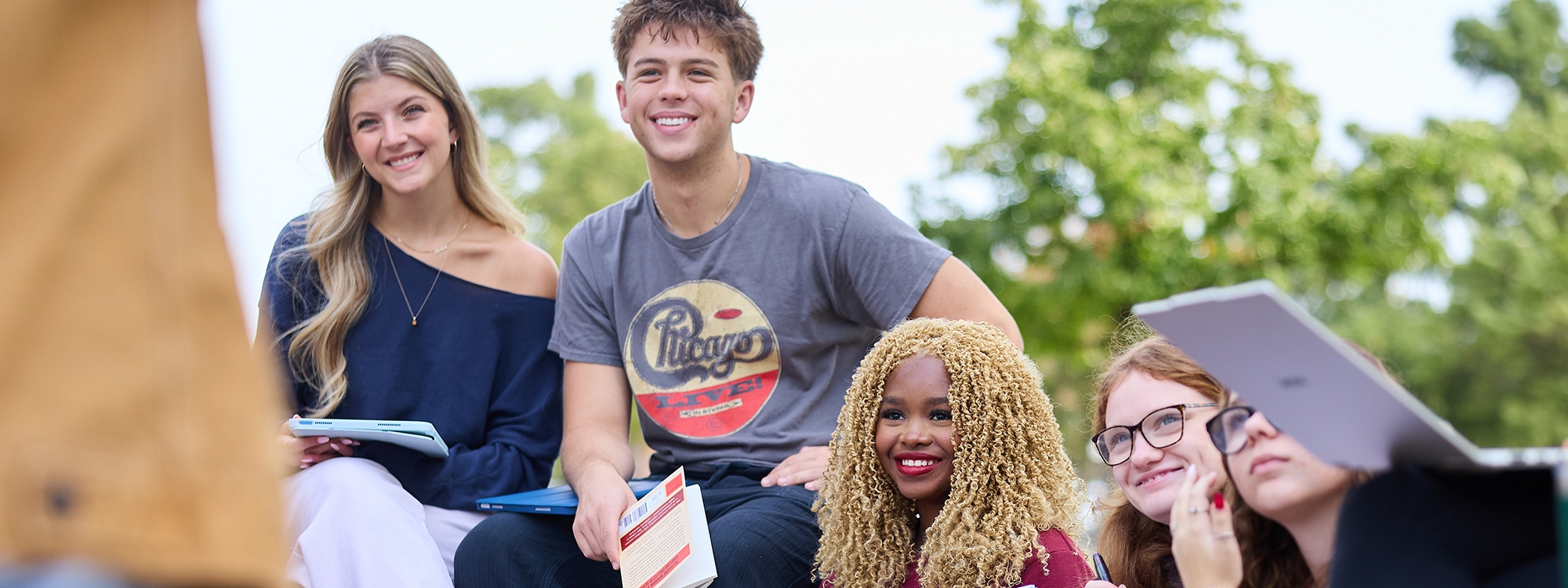 A group of undergraduate students attending a drama class being taught outside.