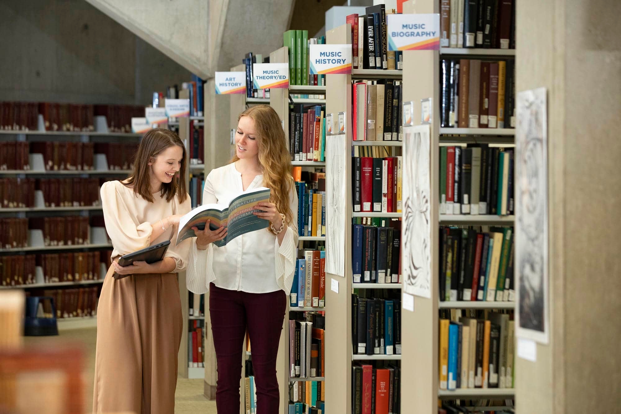 Graduate students looking at book near stacks in Fine Arts Library.