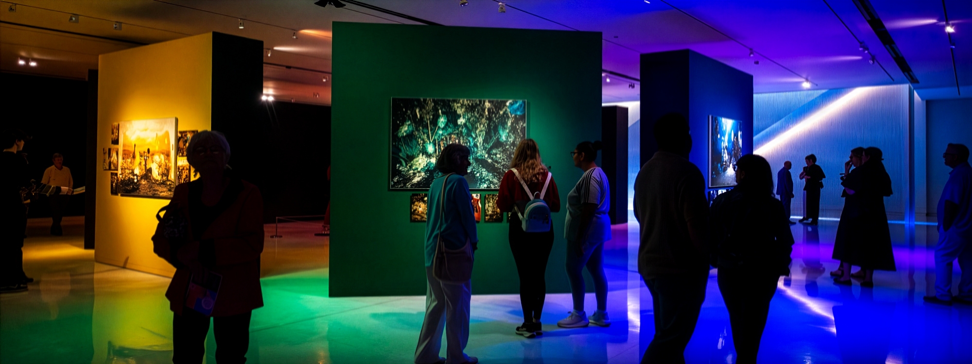 Several people looking at colorful works of art on walls.