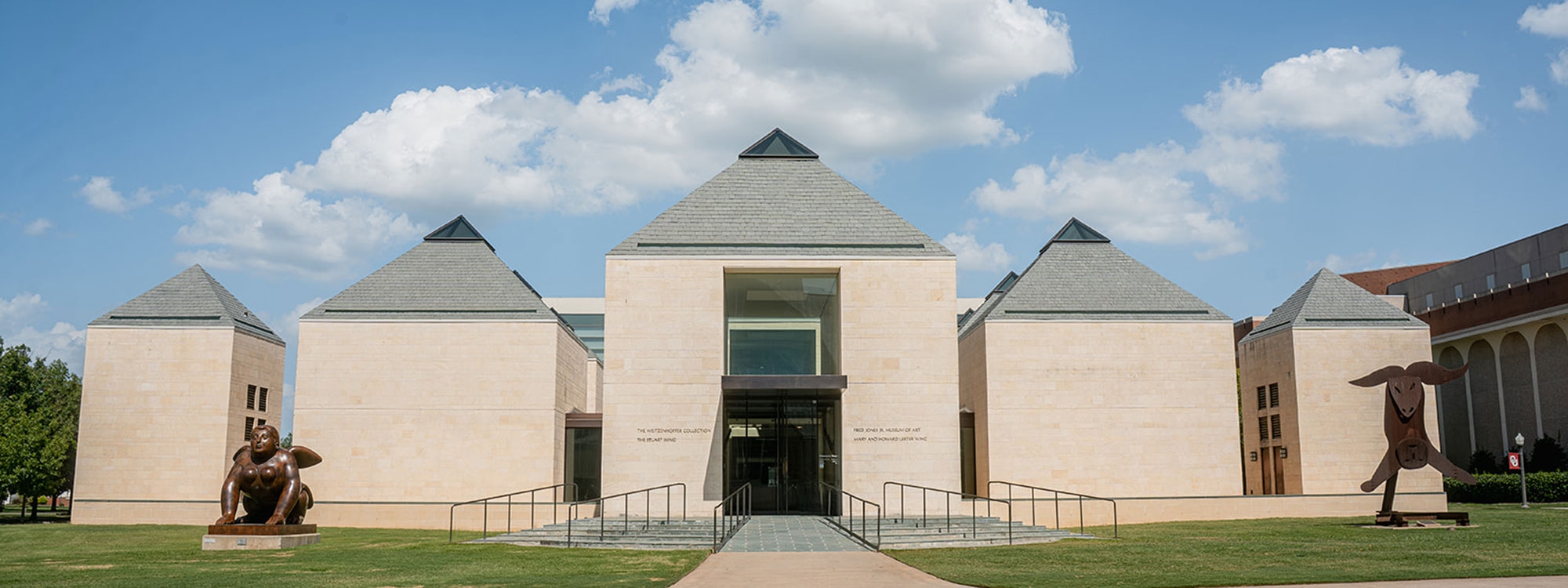 The exterior of the Fred Jones Jr. Museum of Art, with a blue sky and clouds in the background.