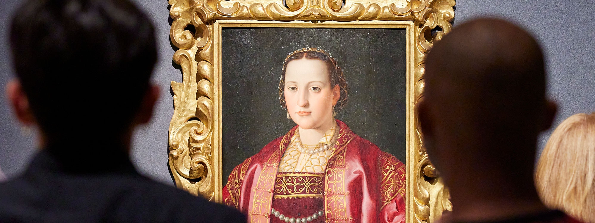 Two people looking at a painting of a woman hanging on a wall.