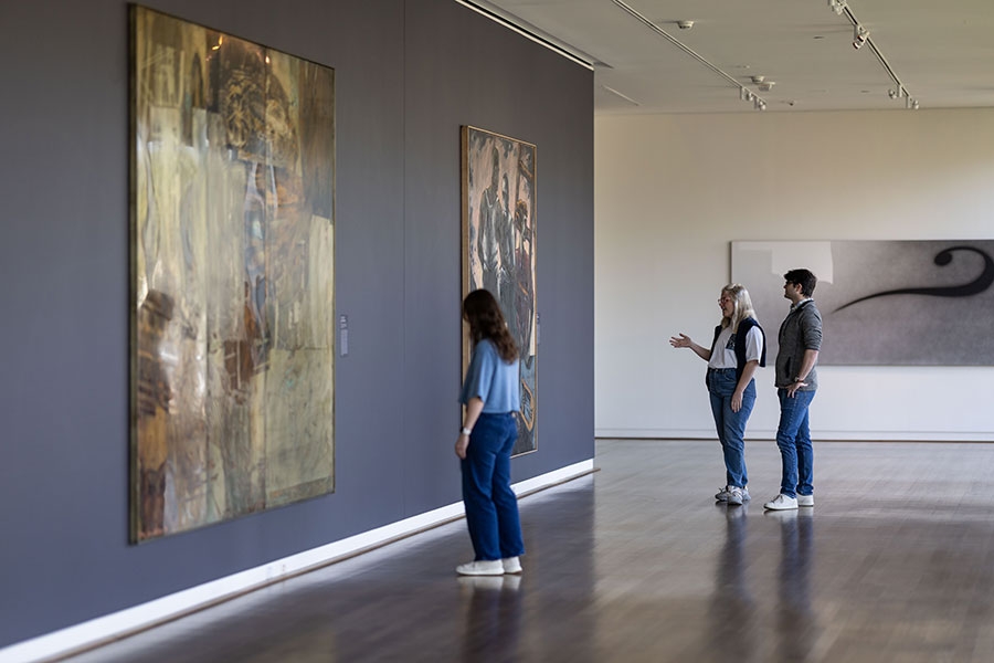 Three museum patrons looking at large pieces of art.