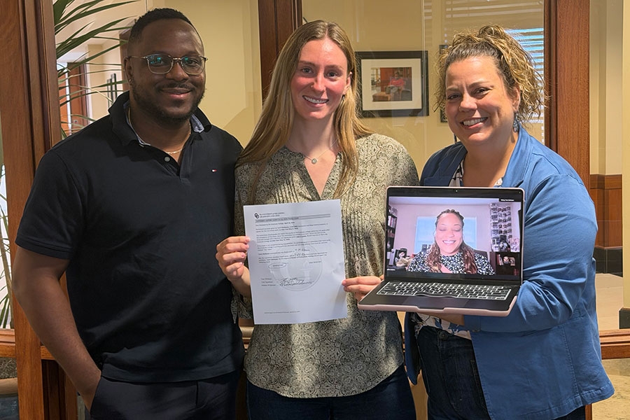 Gaylord faculty and students posing for a photo while holding a laptop and a piece of paper.