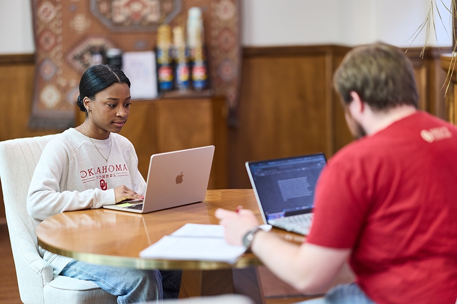 Two students sitting at a table with laptops.