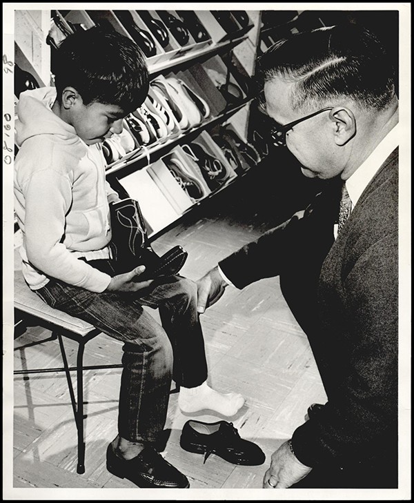 EATON, DAVID: UNKNOWN: Caption reads, Will it be shoes or cowboy boots? Johnny Suke (left), a Kickapoo Indian from Jones, tries to make his choice with the help of David Eaton. Eaton and fellow employees in the Aircraft Branch's service section at Tinker bought shoes for Johnny and the 34 other Indian children from Jones, and turkey dinners for their families. Staff Photo by George Tapscott. Original Photo 12/19/1969. Published on 12-19-69.