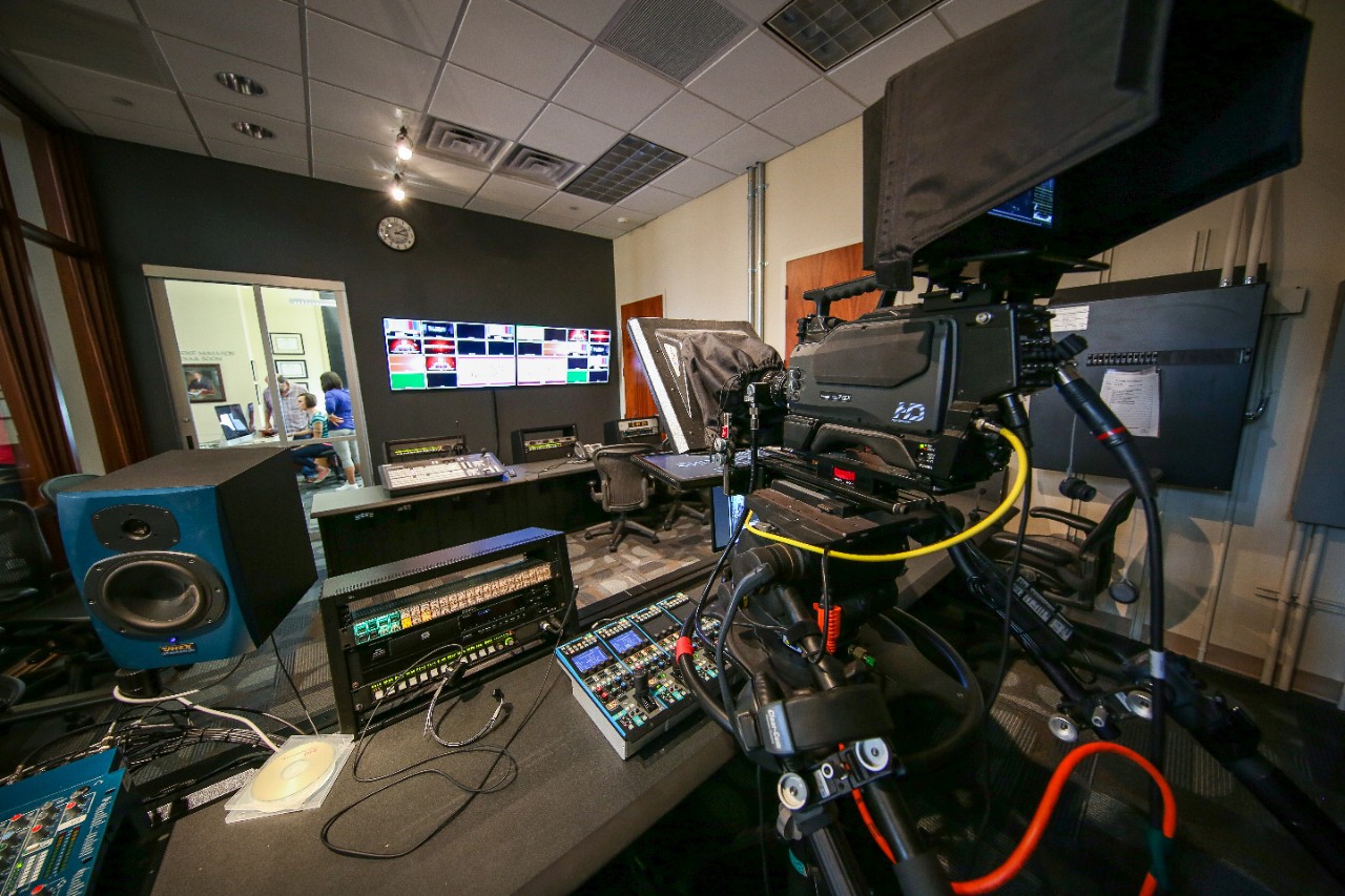 Behind the scenes of a broadcast lab with a camera and control board.