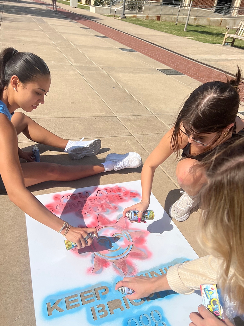 Students paint the sidewalk with an advertisement for 988.