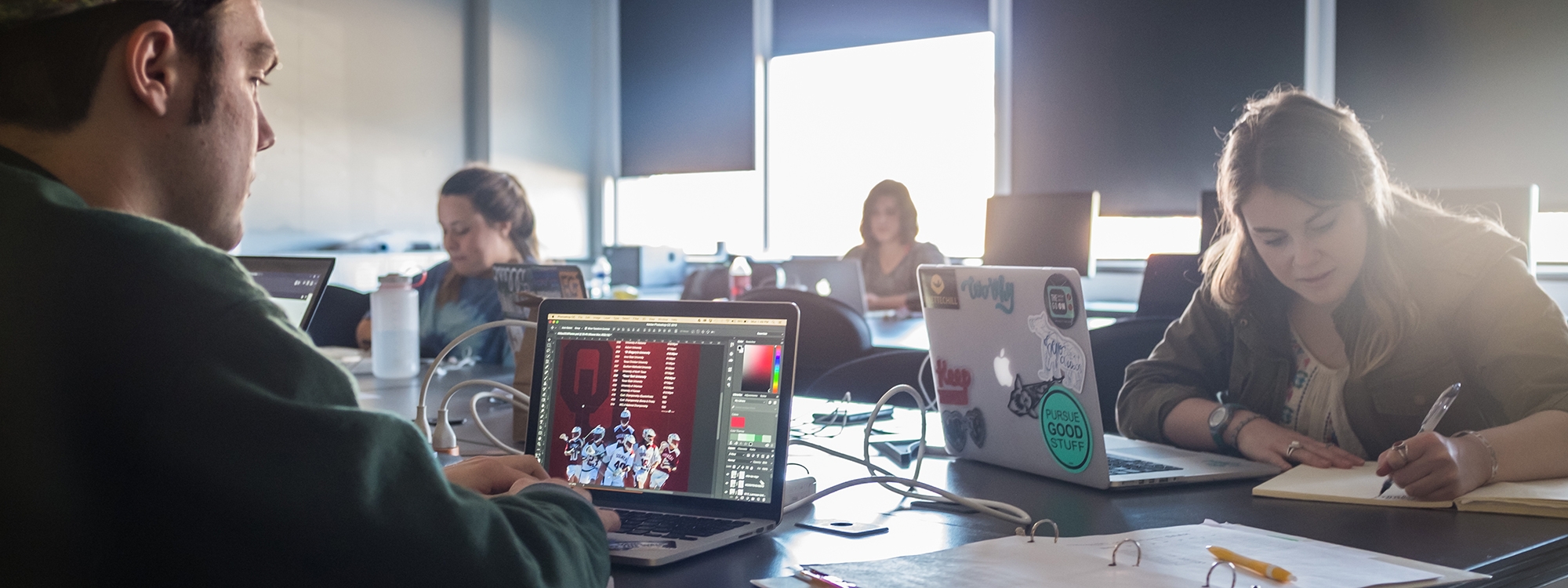 Students working with laptops, books, and notebooks in a computer lab.