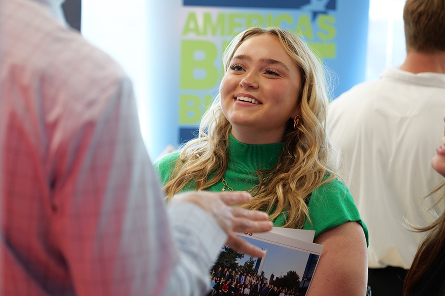 A smiling student speaking to a person at a conference.