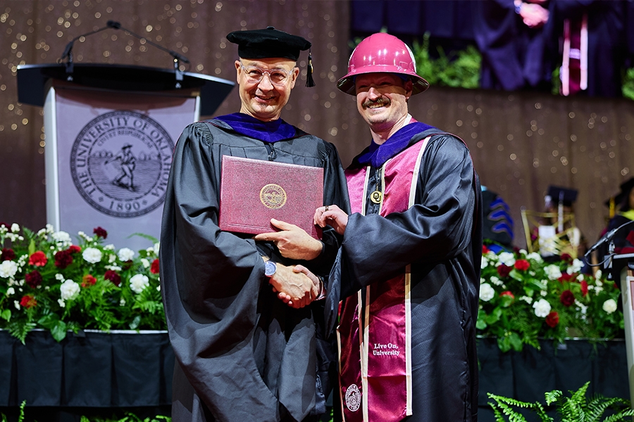 Dean Hans Butzer shakes hands with a construction science student in graduation regalia.
