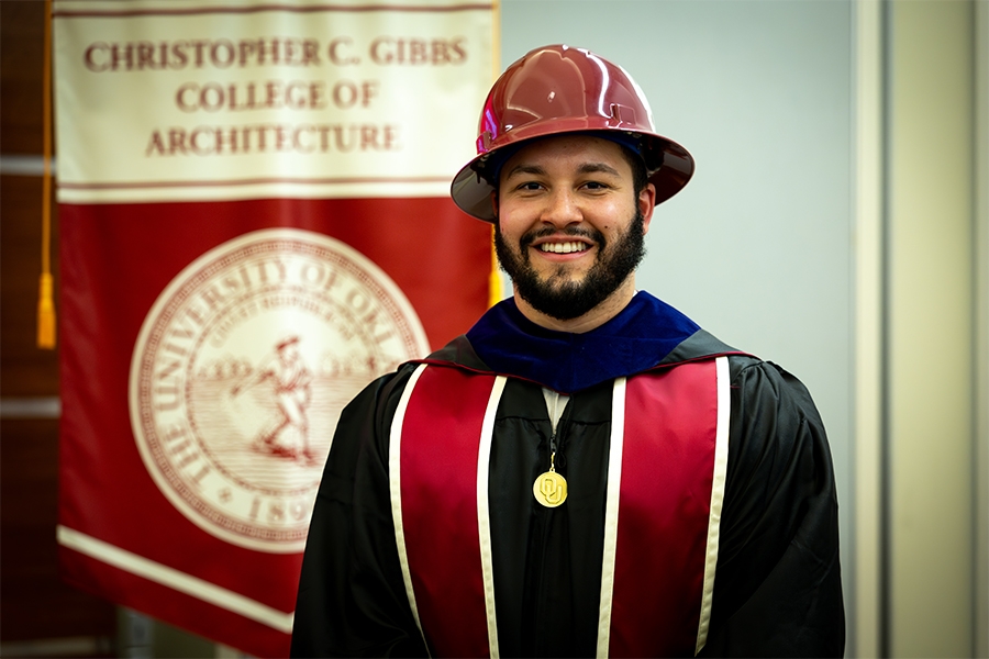 A Christopher C. Gibbs College of Architecture student in graduation regalia, wearing a hard hat.