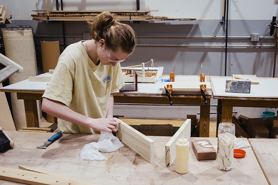 A student working with wood and glue in a workshop setting.