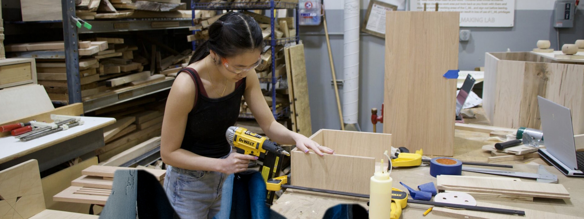 A student using power tools and working with wood in a workshop.