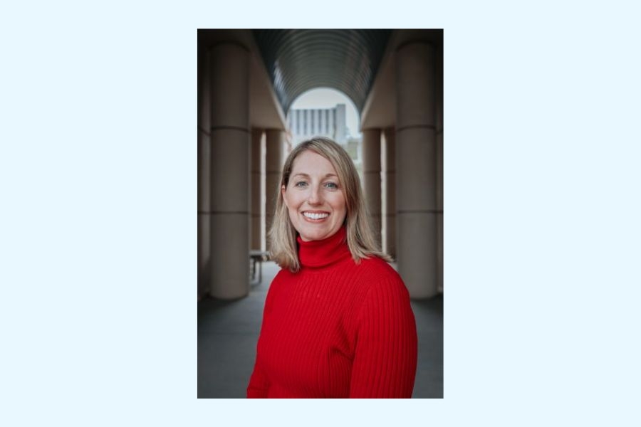 Headshot of a woman in a red long sleeve turtle neck top with an arch in the background