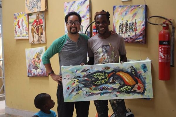 Christopher Le and another man holding painting in studio with child and artworks on wall