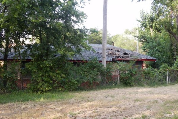 Overgrown abandoned house with damaged roof and trees surrounding yard