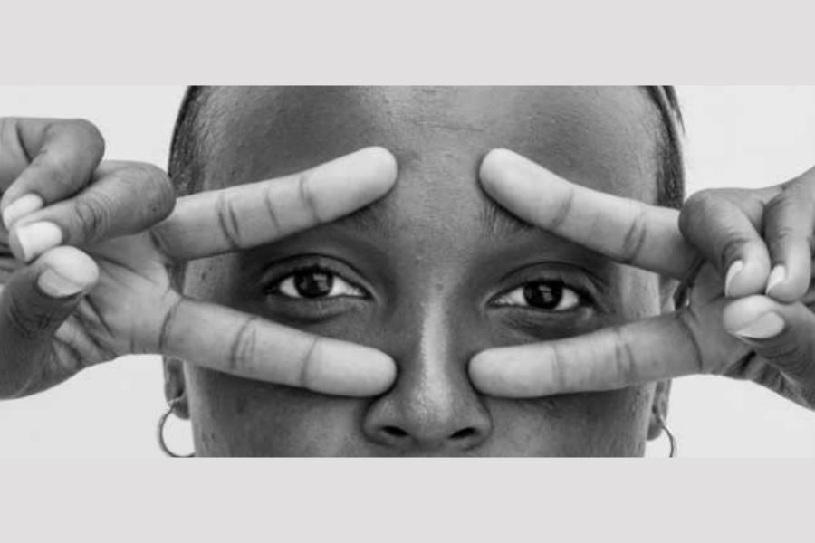 Photo of a woman of color making sideways peace signs against her eyes in a close up profile shot