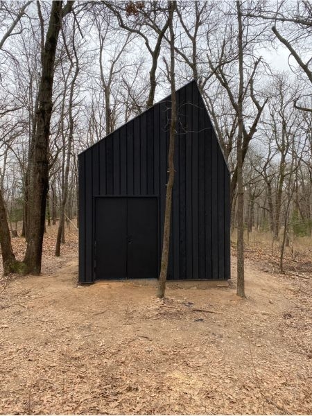 Image of dark grey house structure in the middle of a forrest in winter. 