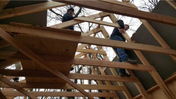 Two people working up in roof scaffolding and wood framing. 