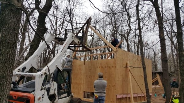Bobcat skid steer helping raise material for roof of wood structure and framing. 