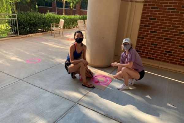 Two masked people painting pink circle stencil on sidewalk