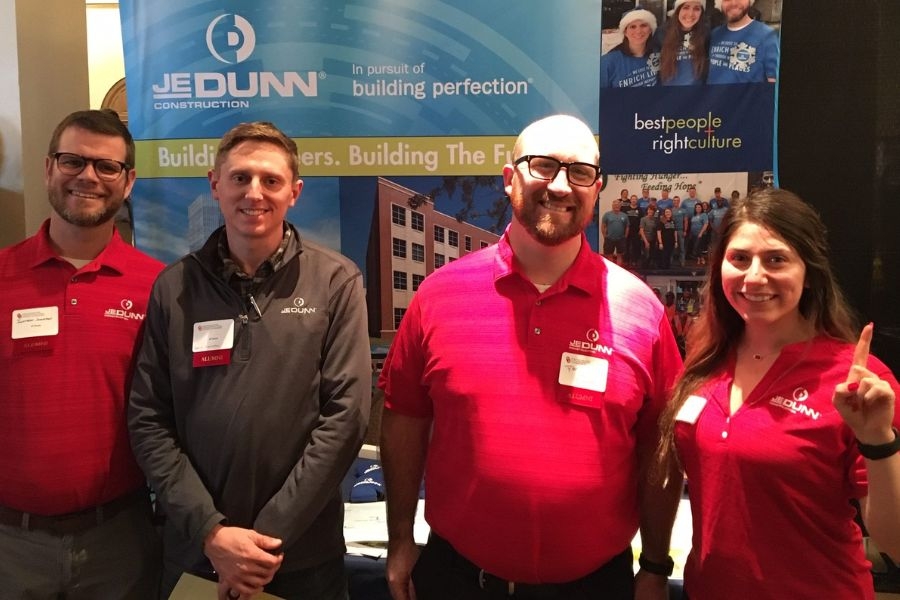 Four professionals standing in front of a booth at a career fair