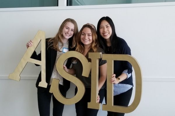 Three students pose with giant a s i d letters