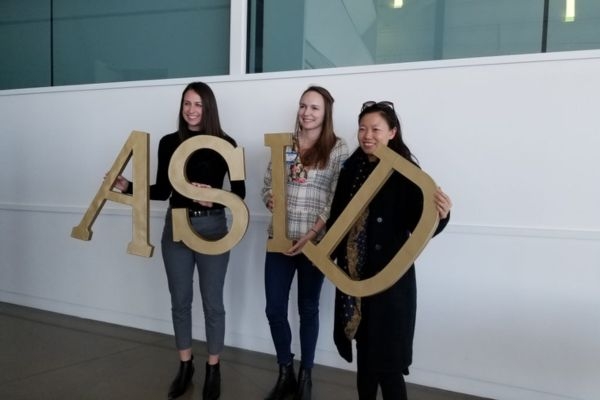 Three students pose with giant a s i d letters