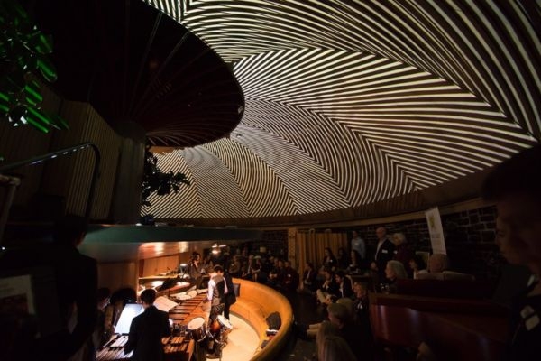 Audience watching musicians beneath striped light projection ceiling