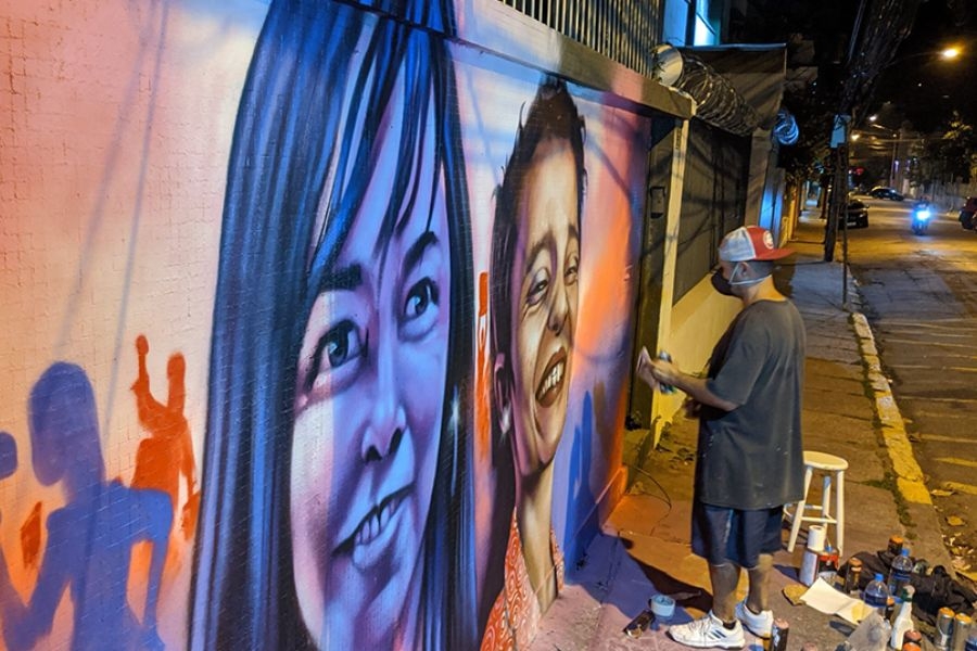 Man painting large colorful portrait mural on city sidewalk at night
