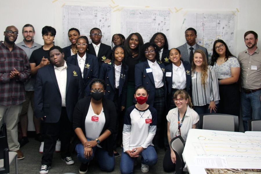 Group of Tulsa students alongside Urban Design students posing in front of a wall with multiple planning posters. 