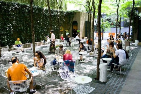 Picture of large outdoor space with plenty of plants and seating at tables for people to gather and hang out. 