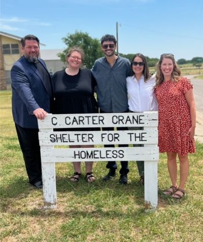 OU research team standing behind white sign for C. Carter Crane shelter for the Homeless.