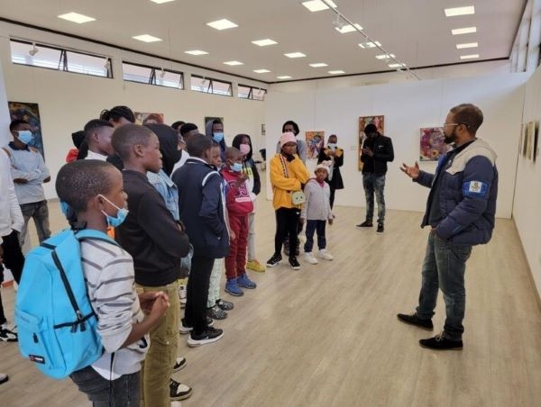 Workshop participants hearing from a prominent Zambian painter at a gallery featuring his work.