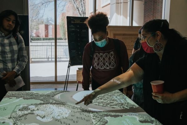 Laura Harjo pointing at a map projected onto a tabletop model.