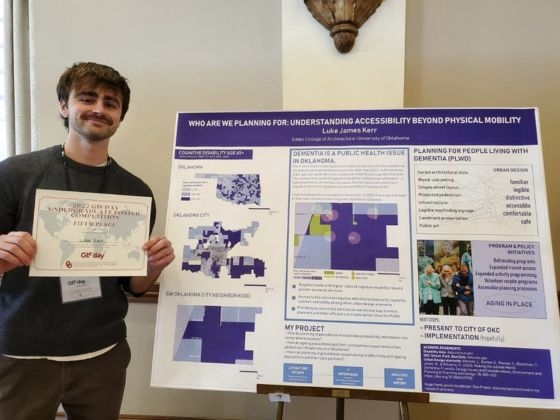 Student Luke Kerr holding fifth place award next to his G I S poster on physical mobility.