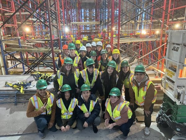 A group of students and professionals in hard hats and hi-vis vests.