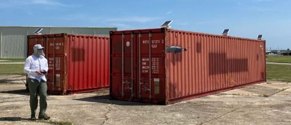 A man flying a drone near two shipping containers.