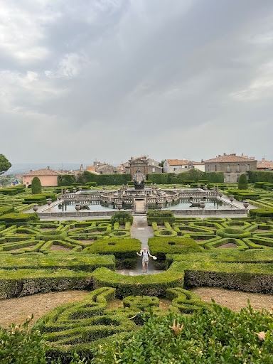 A student standing in a baroque garden with a central fountain.
