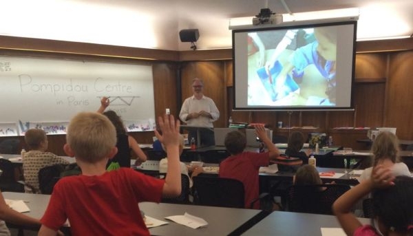 Daniel Butko with a classroom full of grade school students raising their hands.