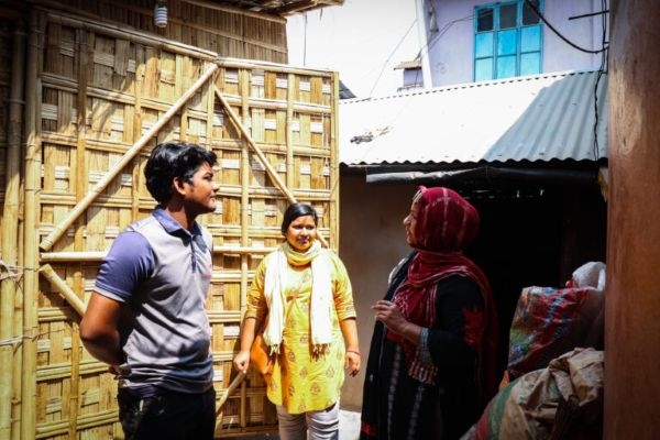 Three people outside of a prefabricated bamboo shelter.