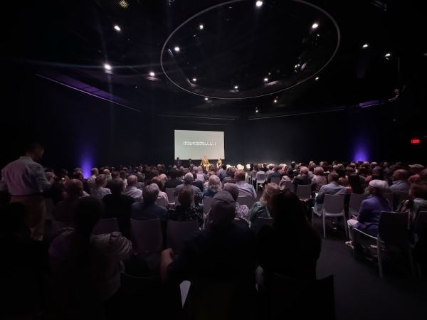 A presentation with a full hall of seated guests.