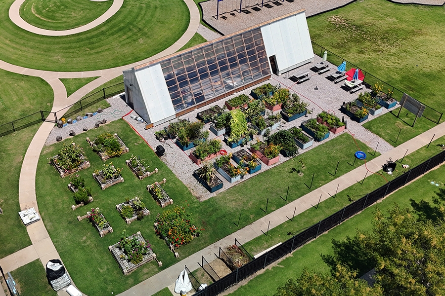 Aerial view of a modular greenhouse with adjacent raised garden beds arranged within a fenced schoolyard