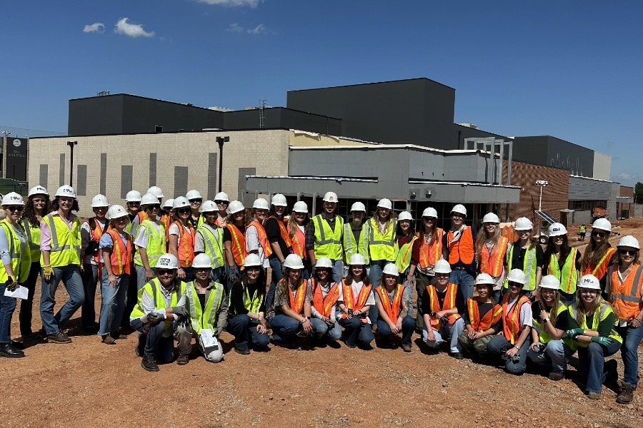 A group of students with hardhats stand outside a construction site. 