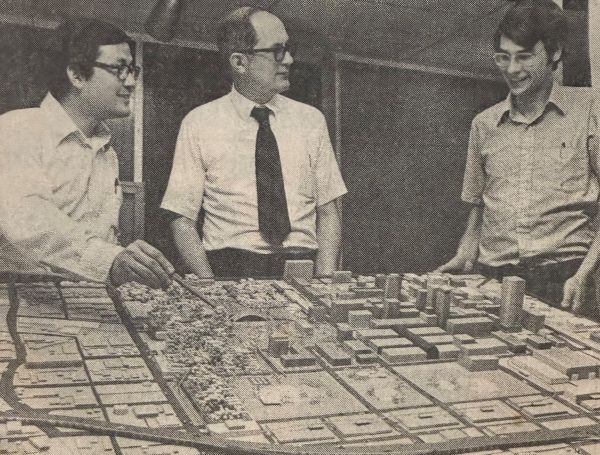 3 men standing around a city model on a table. 