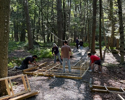 People working on building a wooden frame structure in the woods. 
