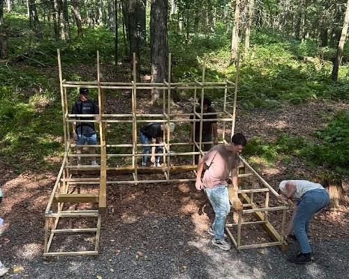 People building a wooden structure in the woods. 