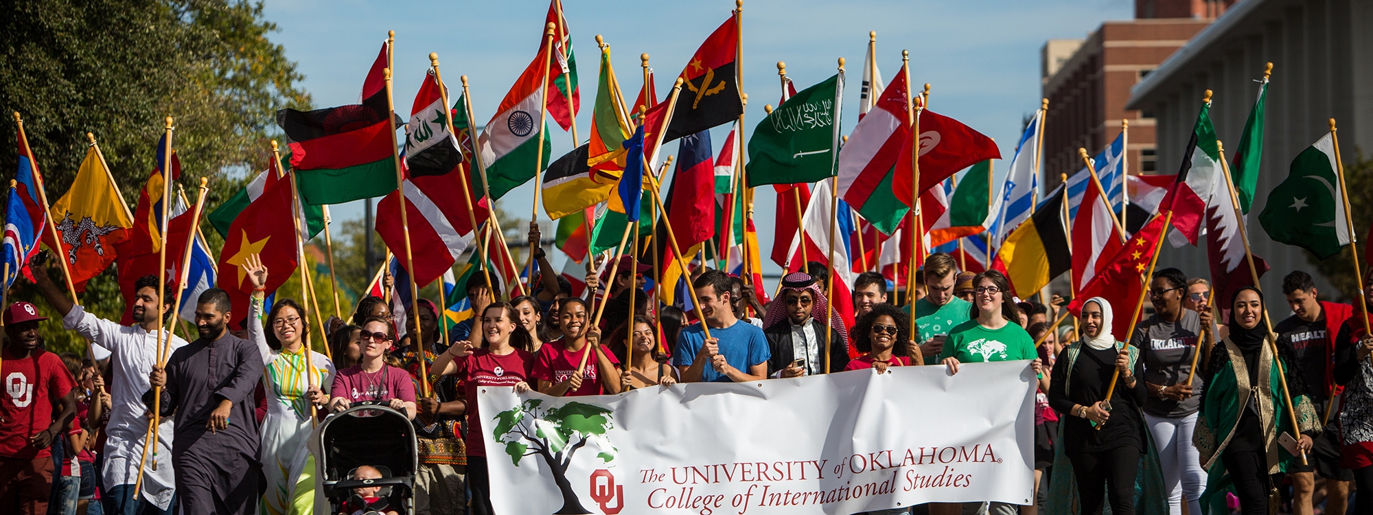 International students walking down Boyd St. in a parade, hoisting flags from countries from around the world.